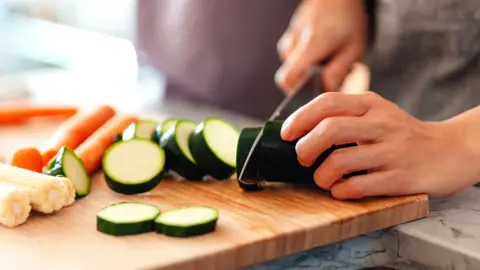 A person at home chops a courgette on a wooden choppin board