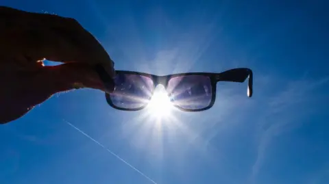 A hand holding up sunglasses against the sun