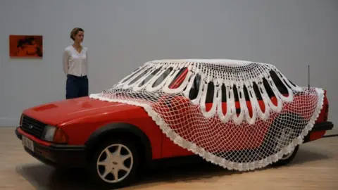 Reuters A gallery assistant poses with Turner Prize shortlisted artist Jasleen Kaur's installation, a doily covered red Ford Escort