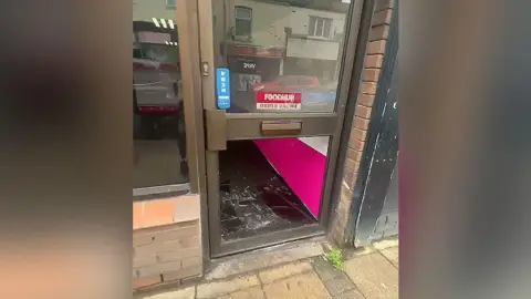 Burger Inc Front door of a takeaway with the bottom pane of glass smashed after a break in. Broken glass is seen on the floor of the premises near the front door. 