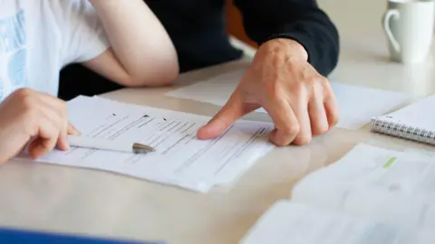 Getty Images A close up of the hands of an adult an child looking at documents on a desk