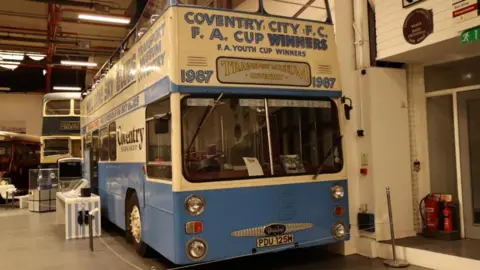 Coventry Transport Museum A blue and cream vintage bus, that open top and has writing on it that reads "Coventry City FC, FA Cup Winners. The bus is in a transport museum.