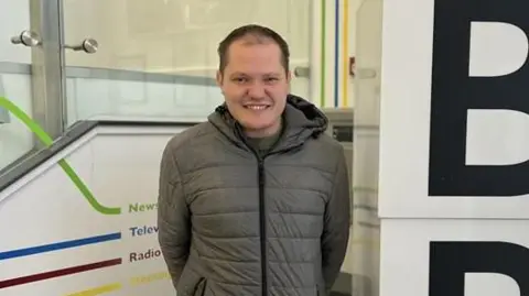 Jake Banbury smiling at the camera and wearing a grey coat.