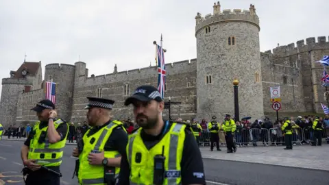 Getty Images Three police officers in high-viz clothing are crossing pictured up close as they cross a road. Windsor Castle is in the background, as well as several other police officers and a cue former by members of the public. 