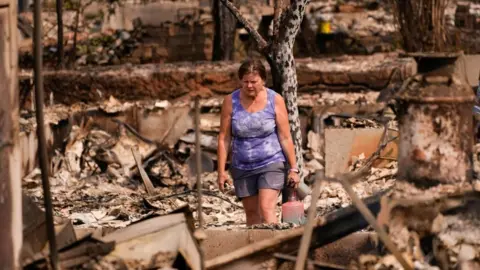 A woman surveys the remains of her home that was burned, in the Old Trails Fire, in Spokane, Washington