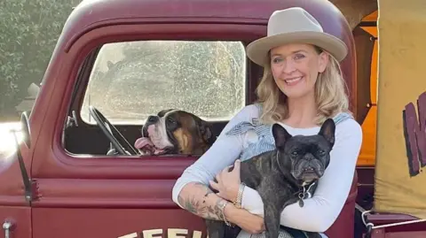 An image of Lynsey Hand wearing a cowboy hat whilst holding a dog with another dog in the vehicle behind her