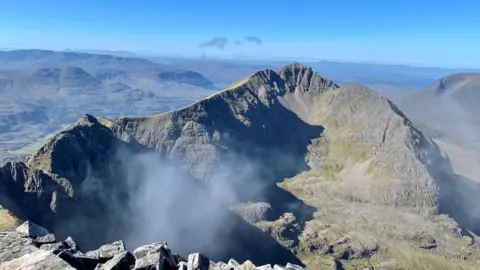 Nigel Patrick A rocky mountain with low cloud and under blue skies