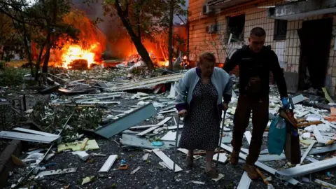 Reuters Uma mulher recebe assistência ao deixar o prédio de apartamentos atingidos durante mísseis russos e ataques com drones em Kiev, Ucrânia, no início da quinta -feira