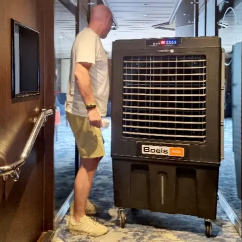 Andy Peach Man walks around a large air conditioning unit in a corridor onboard a cruise ship