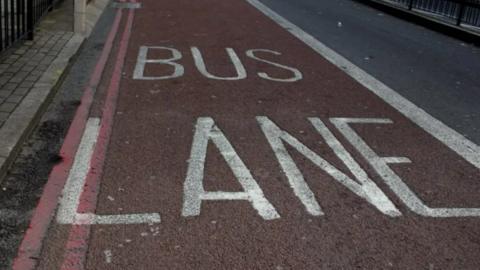 A bus lane seen from above with white writing on dark tarmac