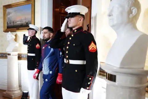 Getty Images A UFC fighter walks through the White House, past two security staff