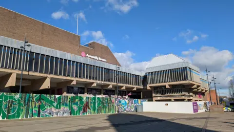 Grey rectangular building with graffiti wall infront and large grey rectangular windows