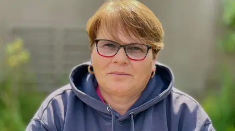 Stephen Huntley/BBC A woman in a light blue hoody and short red hair and glasses.