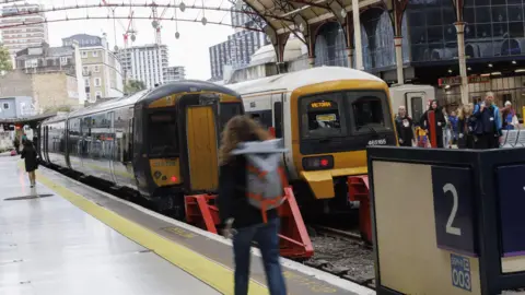 Passengers walk to two trains at Victoria Station with a platform 2 sign in the foreground