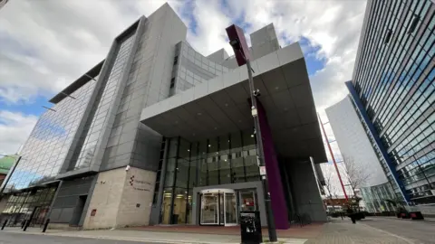 Stuart Woodward/BBC The University of Essex Southend campus main building. Its left-hand wall is covered in windows, and there are grey cladding panels across the curved front of the building. There is an angled grey cover protruding over the main entrance, and a purple cladded tower alongside it.