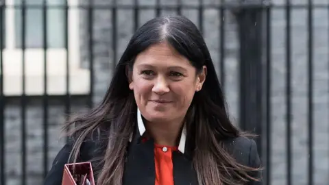 Culture Secretary Lisa Nandy smiling outside Downing Street. She has a black blazer and a red top.