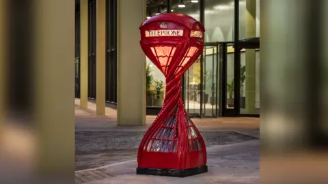 Charles Emerson A red phone box twisted with a light on inside in front of an entrance to a building