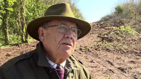 Henry Danter, wearing a brimmed hat and barbour-style jacket on his land