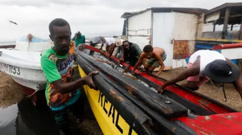 REUTERS/Octavio Jones Men, some wearing t-shirts and trousers and others just shorts, lean in as they pull a boat onto sand.