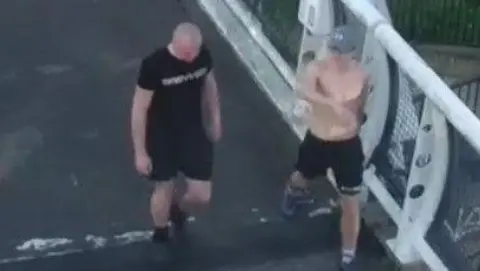 Gloucestershire Police Two men in blurred CCTV footage. One is shirtless, and wears black shorts and a grey cap. The other is bald, and wears a black t-shirt, shorts and trainers. They are on a bridge with white railings. 