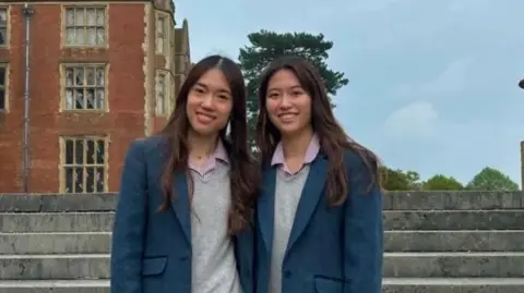 BENENDEN SCHOOL Nicola and Victoria Tsang in their school uniforms smiling.