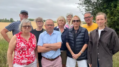 BBC A group of nine people stood together in front of a field, where development is planned.