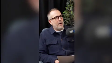 Dr Xand speaks into a microphone while holding a letter