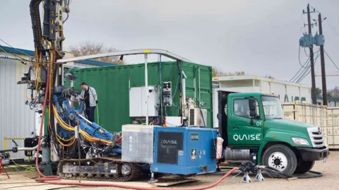 Quaise A drill stands in front of a green truck with the Quaise logo