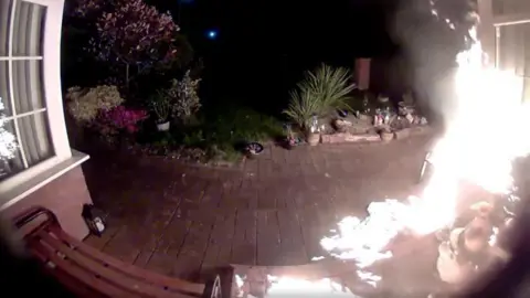 Doorbell footage shows the outside of a home, with a fire lit up to the right hand side. 