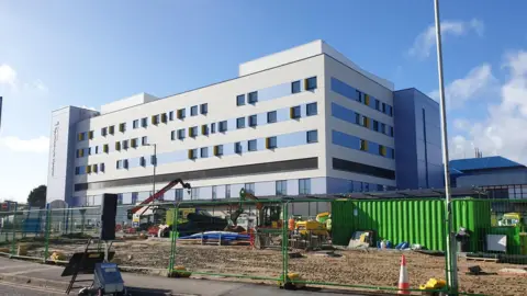 Exterior shot of the BEACH building at Bournemouth Hospital. There are road and landscaping works going on in front of the building as it nears completion.