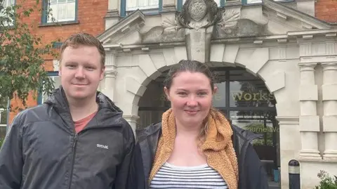 Ashley Gurr and Niamh Gillen stand outside Barbourne Works in the rain, wearing waterproofs, after they left the building. 