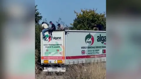 Submitted Still from a video showing three men on top of the roof of a lorry