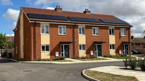 BBC/Matt Knight A picture showing three modern terraced houses in St Michaels Place in Chelmsford with solar panels on their roofs.