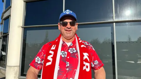 Leonard Gregory dressed in sunglasses, a red Hawaiian shirt, blue baseball cap and Hull KR scarf 