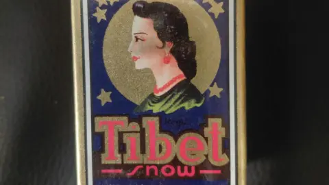 Luton Borough Council A packet with a drawing of a woman's face on it, with a red necklace, red earrings, red lips and long dark hair. It says Tibet snow.
