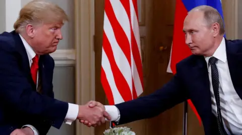 Reuters Trump on the left and Putin on the right shake hands. They two are not smiling but rather pursing their lips and narrowing their eyes. The Russian and US flags are behind them. 