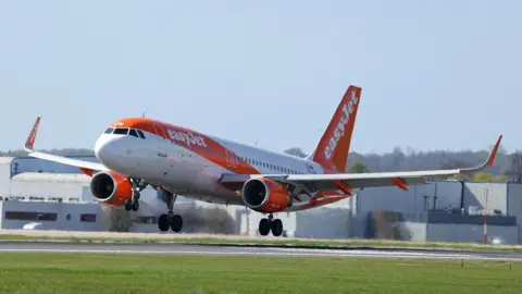 A white and orange easyJet plane landing on a runway.