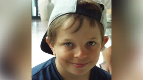 Brain Tumour Research Finaly Church, a young boy is wearing a dark blue T-shirt and a backwards light grey cap and is looking at the camera with a slight smile on his face. 