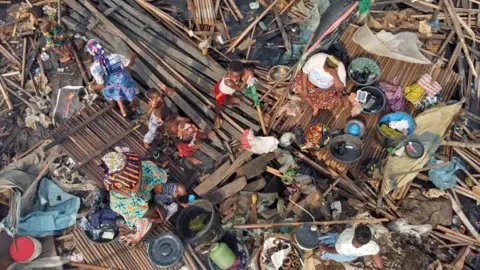Gift Ufuoma/BBC A birds-eye view of women and children sitting on wooden debris in Makako slum.