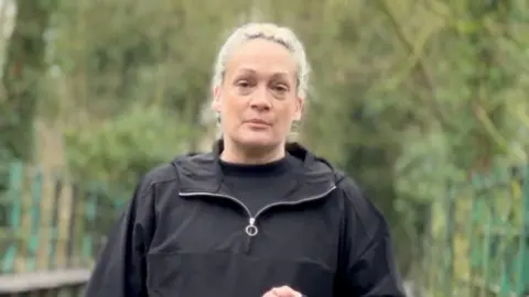 Contributed Mrs Blezard looks at the camera while standing outside. She wears a black jacket with a black top underneath. Trees can be seen behind her.