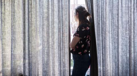 Woman staring through partially closed curtains