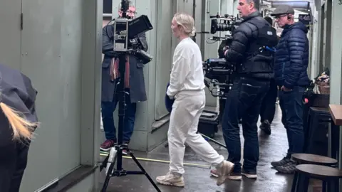 Neve Gordon-Farleigh/BBC Holliday Grainger in a white tracksuit filming in Norwich Market.