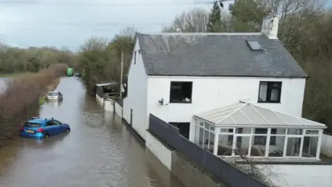 A view of the outside of the house showing flood waters submerging cars. 