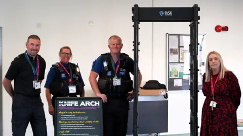 Members of the police and school staff stood next to the black knife arch which looks like an airport metal scanner
