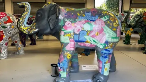 Slough landmarks drawn on the elephant Hope. It shows the McLaren car and a telescope with other designs. Sunflowers are scattered all over the elephant. 