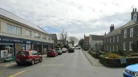 A view of the high street in St Martin showing a road with houses along either side and cars travelling down the road. 