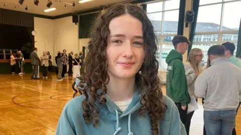 Grace McMullan, with long curly brown hair and wearing a blue hoodie, at Down High School