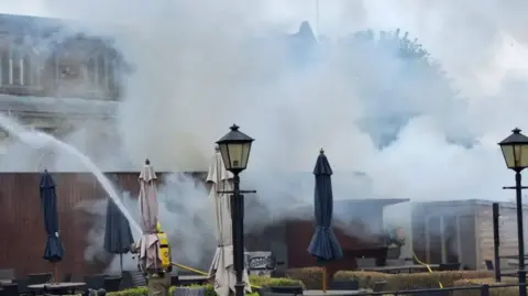 Leicestershire Fire and Rescue Smoke in the garden of the Tithe Barn in Cosby with hoses spraying water.