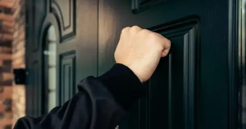 Getty Images A man's arm outstretched to knock on a black front door
