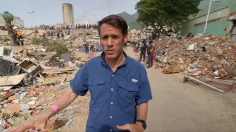 Man in blue shirt walking among rubble after earthquake